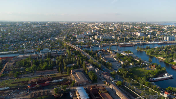 Aerial view of the Kherson city. A shipyard on the banks of the Dnieper River of which there are cranes and ships. Residential area with houses and greenery